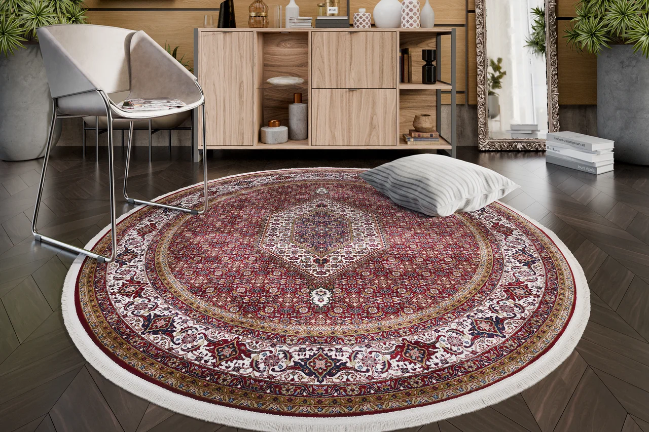 Ein traditioneller, klassischer, roter, runder Teppich mit Fransen liegt im Wohnzimmer auf dem Boden. - Ein traditioneller, klassischer, roter, runder Teppich mit Fransen liegt im Wohnzimmer auf dem Boden.